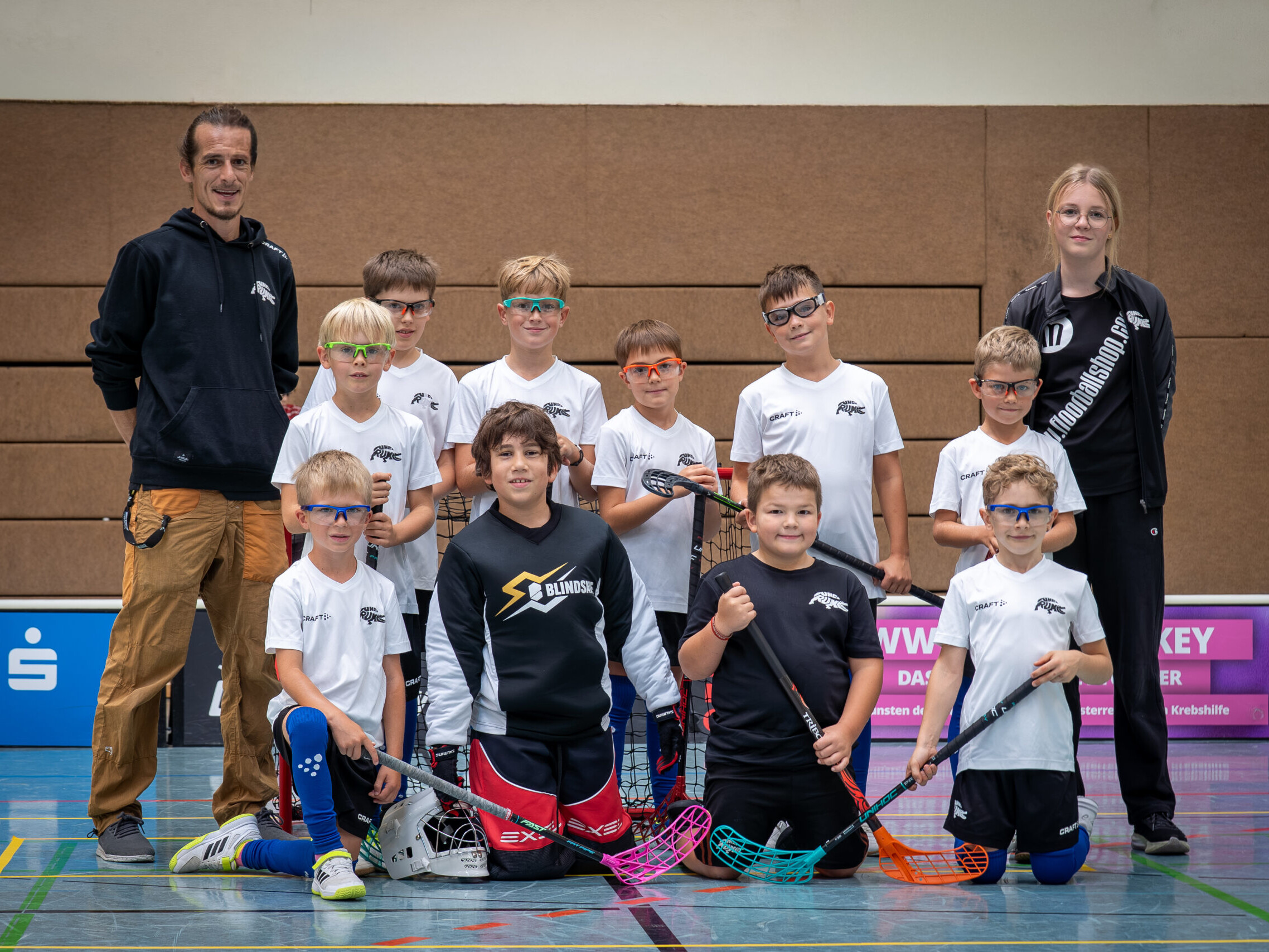 Junge Floorballer mit weißen Dressen und Trainerteam beim Mannschaftsfoto