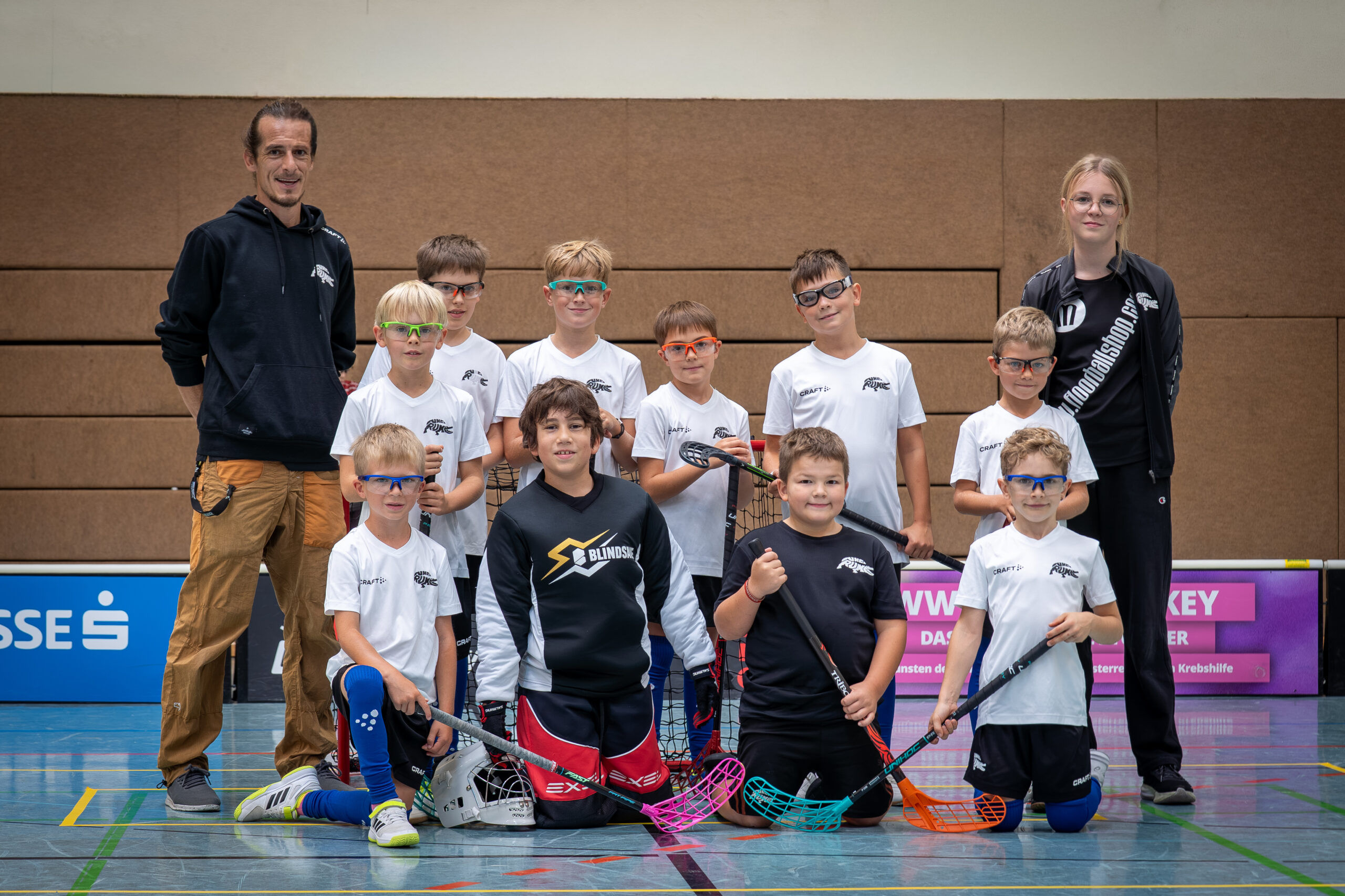 Junge Floorballer mit weißen Dressen und Trainerteam beim Mannschaftsfoto